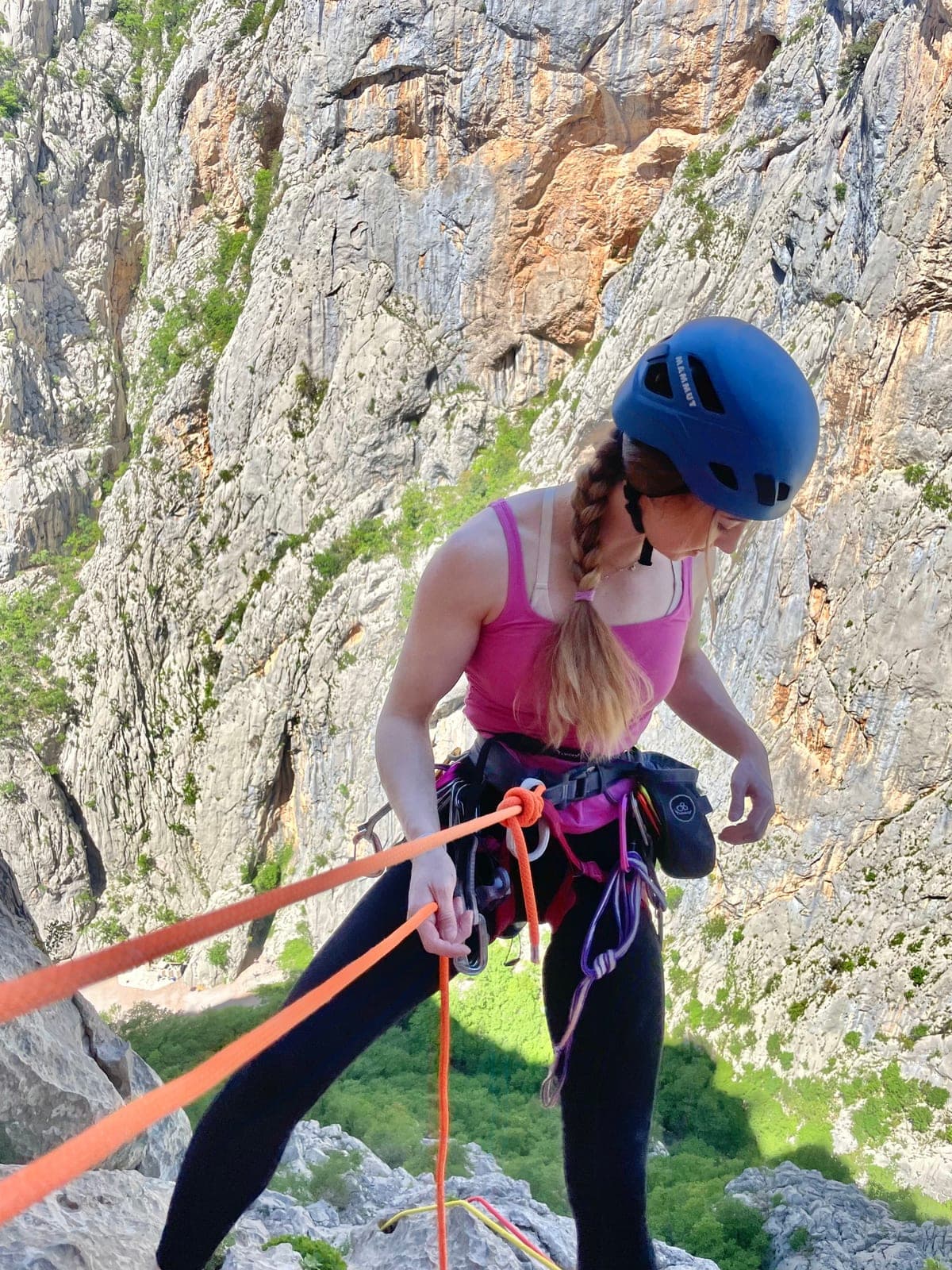 Urška in a helmet, rappelling on a sunny rock face