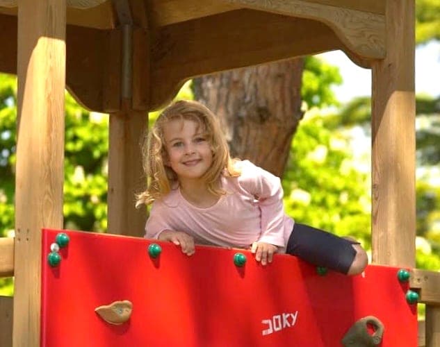 Urška as a little girl, peeking over a red climbing wall on a playground
